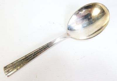 une cuillère en argent à long manche posée sur une surface blanche