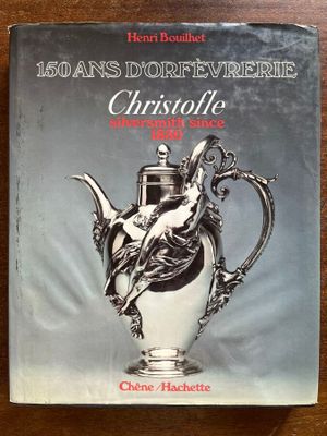 un vieux livre sur lequel repose une théière en argent, posé sur une table en bois