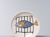 une petite assiette sur laquelle est posé un poisson, posée sur une table