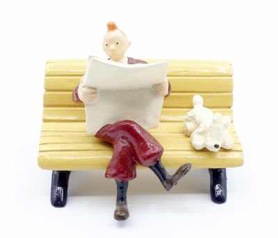 a figurine of a man sitting on a bench reading a newspaper