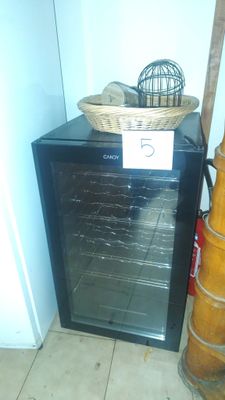 a small black refrigerator with a basket on top of it next to a broom