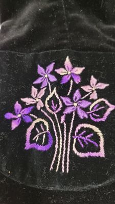 Des fleurs violettes sont brodées sur un sac en velours noir posé sur une table