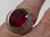 a man ' s hand holding a ring with a red stone on it
