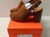 une paire de mules en daim marron à talon en bois, posée sur une boîte orange