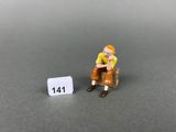 figurine miniature représentant un homme assis sur un banc à côté d'un panneau