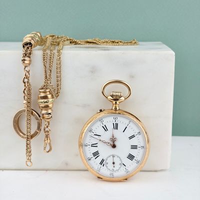 une montre de poche en or et une chaîne en or posées sur un bloc de marbre
