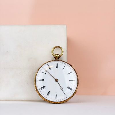 une vieille montre de poche posée sur un bloc de marbre près d'un mur rose