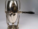 une cafetière en argent avec une anse, posée sur une table blanche