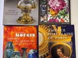 quatre livres posés sur une table, sur laquelle se trouvent également des vases et des tableaux