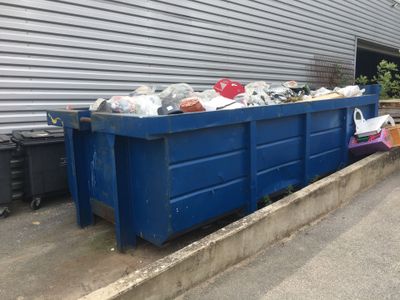 une benne bleue garée devant un immeuble