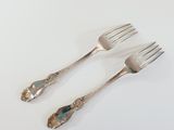 two forks and a spoon on a white table