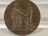 an antique bronze medal with a woman shaking hands with a man