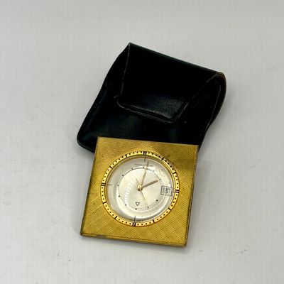 une petite horloge dorée au boîtier noir, posée sur une table blanche