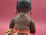 an image of a small doll sitting on a pink surface