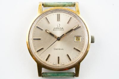 une montre en or avec un bracelet vert sur une surface blanche
