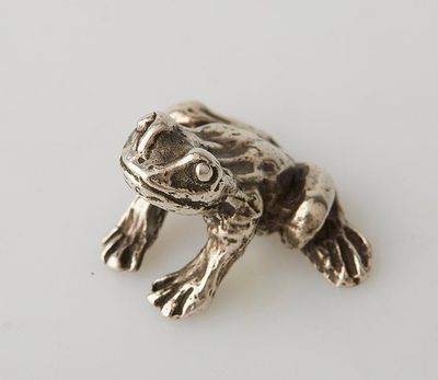 a close up of a silver frog on a white surface