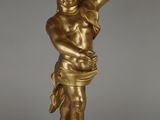 une statue en or représentant un enfant tenant un oiseau, posée sur un socle noir