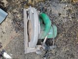 a green circular saw sitting on the ground next to a piece of metal