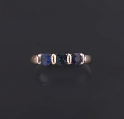 a gold ring with three blue sapphire stones on a black surface