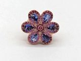 un gros plan d'une bague ornée d'une fleur violette et bleue sur un fond blanc