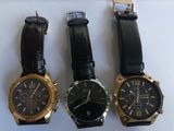 three watches are sitting on a white surface, one is black and the other is gold