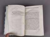 someone is holding a book open on a table with a hand pointing at it