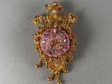 une broche rose et dorée surmontée d'une couronne