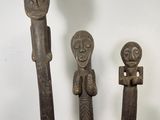 trois statues en bois représentant des personnages, posées sur un socle blanc