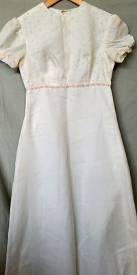La robe est blanche et ornée de passementeries roses.