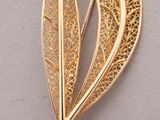 a close up of a gold brooch with a leaf on it