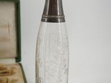 a glass bottle with a silver lid next to an open box