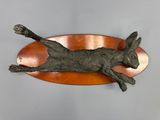 a sculpture of a cat laying on top of a copper plate