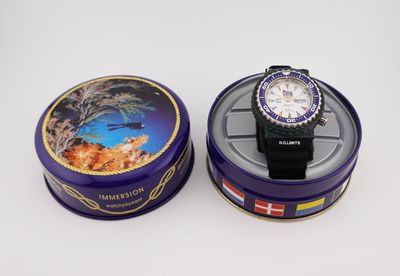 une boîte en fer-blanc violette contenant une montre, posée sur une surface blanche