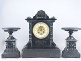 une horloge noire posée sur une table, à côté de deux bougies