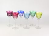 six verres à vin de couleurs différentes alignés sur une surface blanche