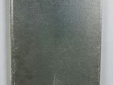an old silver book sitting on top of a table next to a white wall
