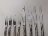 six silverplated knives are lined up on a white surface