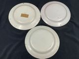 three white plates with gold labels on them sitting on a black surface