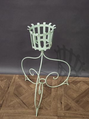 un support à plantes en métal vert, surmonté d'un panier, posé sur un parquet