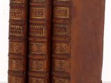 trois vieux livres sont empilés sur une surface blanche