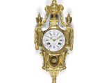une horloge dorée accrochée à un mur blanc, sur laquelle est représentée une couronne