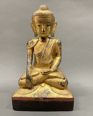 a gold statue of a buddha sitting on a wooden base