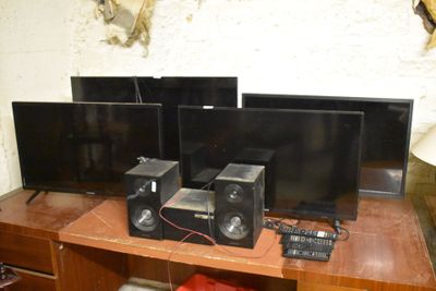 trois téléviseurs posés sur une table en bois sur laquelle se trouvent des haut-parleurs