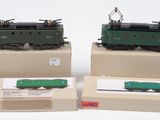 trois trains miniatures sont exposés dans des boîtes posées sur une surface blanche