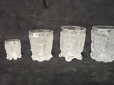 four clear glass vases sitting next to each other on a black surface