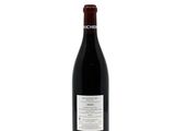 the bottle of red wine is sitting on a white surface