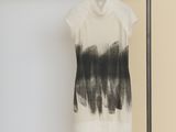 black and white t - shirt hanging on a hanger in front of a yellow wall