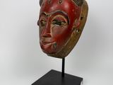 un masque en bois au visage rouge posé sur un socle noir