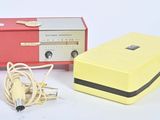 une radio jaune et rouge et un chargeur posés sur une surface blanche