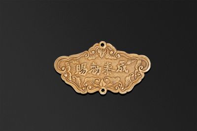 une assiette en or sur laquelle figure une inscription en chinois, posée sur un fond noir